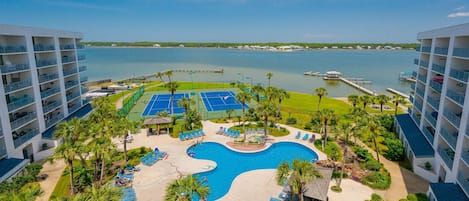 Un resort con piscina central, canchas de tenis y vistas al agua.