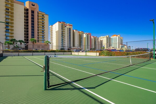 A tennis court with a net, surrounded by buildings and a clear sky. - Phoenix Iv 4072 1 Bedroom Condo (Orange Beach)