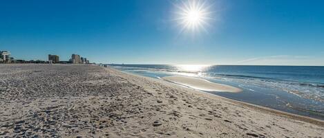A beach with footprints, a clear sky, and buildings in the background.