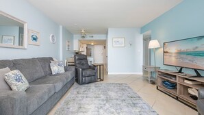 A living room with a grey sofa, a black recliner, a TV, and a painting of a beach scene.
