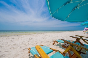 Une plage avec un ciel dégagé, un rivage sablonneux et des chaises longues en bois.