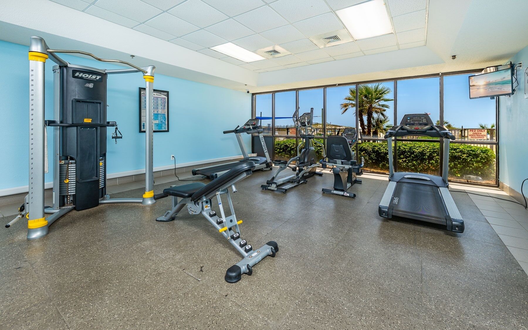 A gym with treadmills, ellipticals, and weight machines, large windows with a view, and a ceiling with recessed lighting.