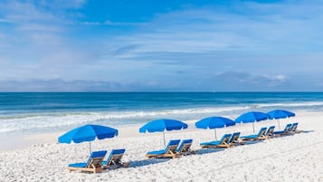 A beach with rows of blue sun loungers and matching umbrellas, arranged on a sandy shore.