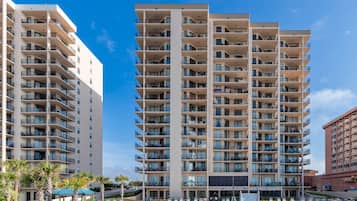 A multi-story hotel with balconies, a pool area, and a beach view.