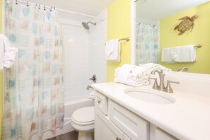 Un baño con cortina de ducha, inodoro, lavamanos y toallero.
