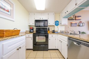 Una cocina con armarios blancos, microondas, estufa y lavavajillas.