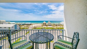 A balcony with a table and chairs, overlooking a beach and buildings. - Gulf Shores Surf & Racquet 612a 1 Bedroom Condo (Gulf Shores)