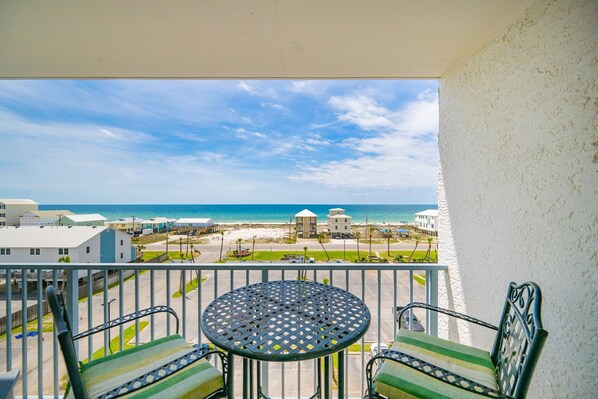 Un balcón con mesa y sillas, con vistas a la playa y edificios.