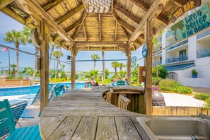 A wooden deck with a pool and bar area, overlooking a pool with lounge chairs and palm trees.