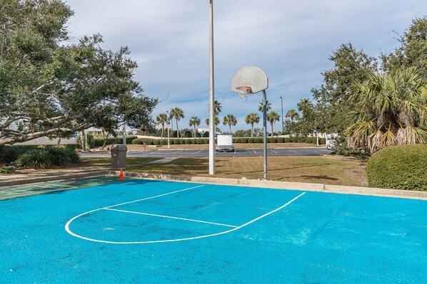 Una cancha de baloncesto con aro, rodeada de árboles y un estacionamiento.
