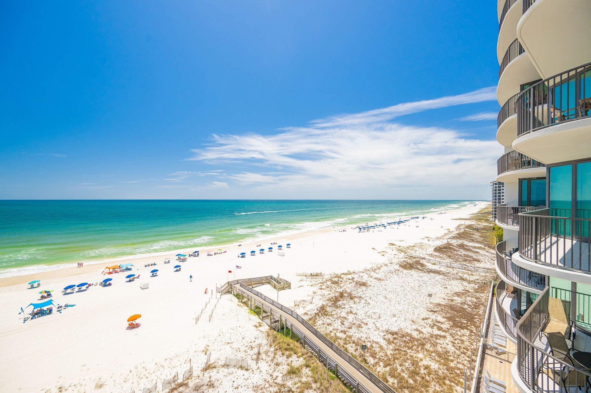 A beach with a wooden boardwalk leading to the shore, a sandy beach, and a building with balconies overlooking the beach.