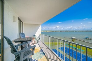 A balcony with chairs and a table, overlooking a body of water and a dock.