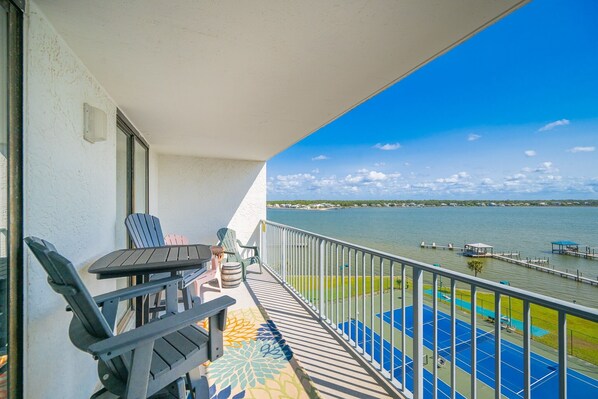 A balcony with chairs and a table, overlooking a body of water and a dock. - Gulf Shores Surf & Racquet 702b 2 Bedroom Condo (Gulf Shores)