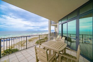 A balcony with a table and chairs, overlooking a beach with umbrellas and people. - The Oasis 406 Formerly Phoenix West Ii 406 3 Bedroom Condo (Orange Beach)