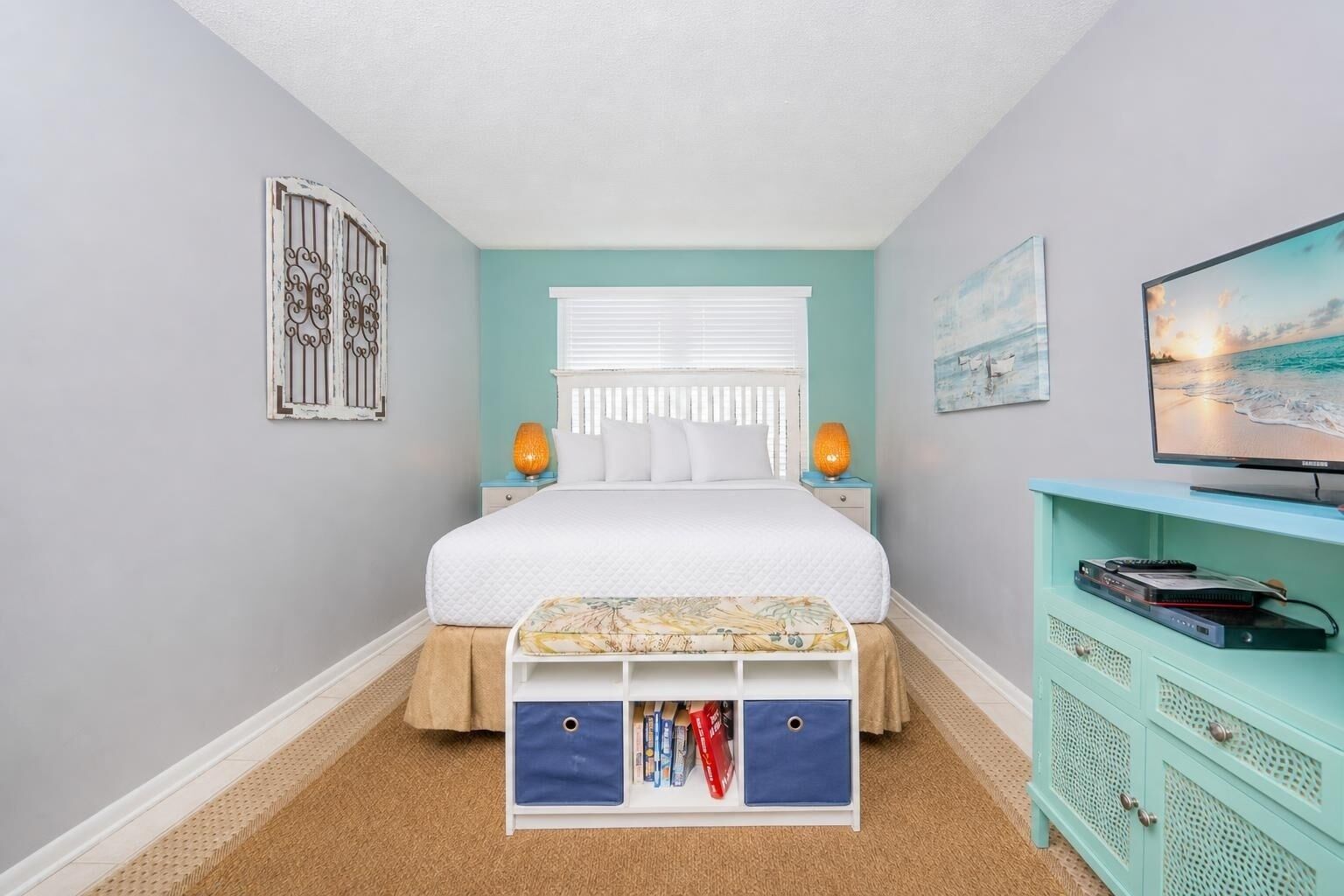 Une chambre à coucher comprenant un lit, des lampes de chevet, un téléviseur, un meuble de rangement et une fenêtre avec des stores.