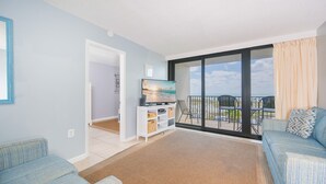 Ein geräumiges Wohnzimmer mit einer großen Schiebeglasdoor, die auf einen Balkon mit Sitzgelegenheiten im Freien führt.