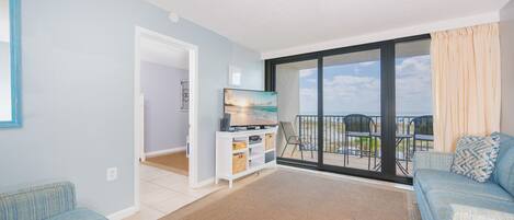 A spacious living room with a large sliding glass door leading to a balcony with outdoor seating.