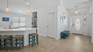 Una cocina moderna con una isla blanca, taburetes de bar, luces colgantes y un refrigerador.
