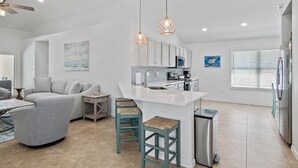 Una cocina moderna con armarios blancos, una isla central y un comedor con sofá gris y taburetes de bar.