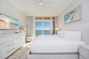 A hotel room with a large bed, a TV, a ceiling fan, and a view of the ocean. - Phoenix Orange Beach 1604 3 Bedroom Condo (Orange Beach)