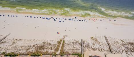 An aerial view of a beach with rows of umbrellas, a swimming pool, and a lifeguard tower.