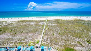 Une plage avec un long sentier menant à un bâtiment doté d’une terrasse et de parasols.