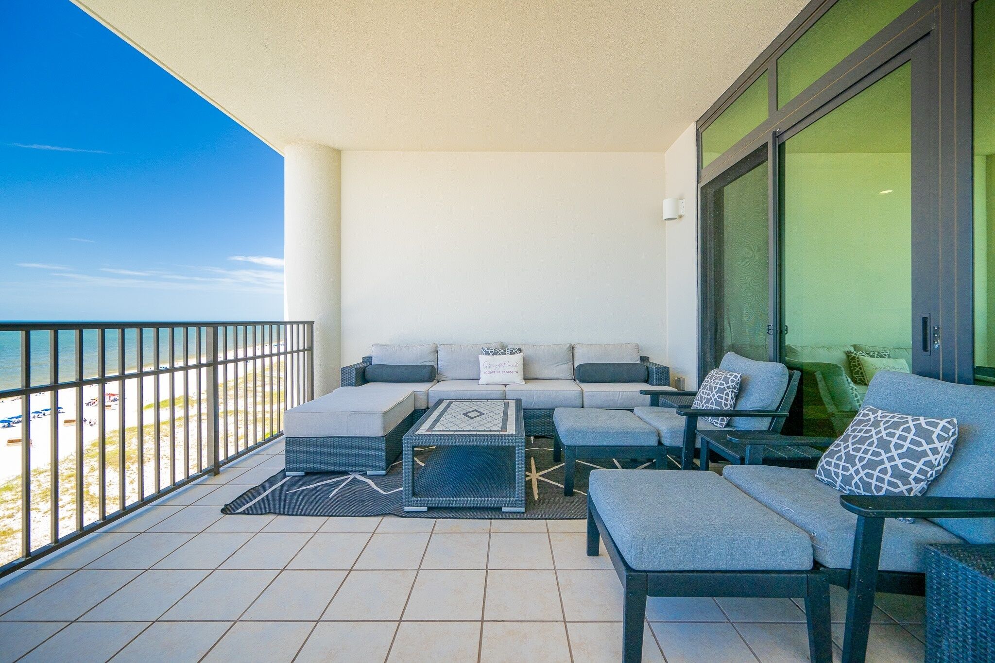 A balcony with outdoor furniture, including sofas and a coffee table, overlooking a beach.