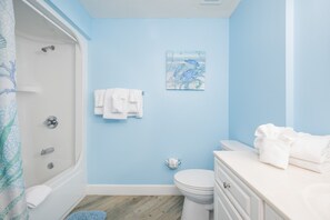 A bathroom with a shower, toilet, and sink, featuring a light blue wall and a towel rack. - Phoenix On The Bay 1223 2 Bedroom Condo (Orange Beach)