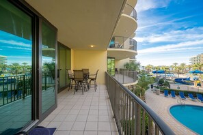 A balcony with a pool view, outdoor seating, and a clear sky. - Phoenix On The Bay 1223 2 Bedroom Condo (Orange Beach)