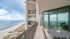A balcony with a view of the beach and ocean, a table with chairs, and a railing.