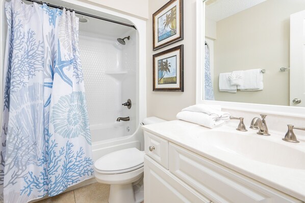 A bathroom with a bathtub, toilet, and a vanity with a mirror and sink. - Phoenix West 1002 3 Bedroom Condo (Orange Beach)