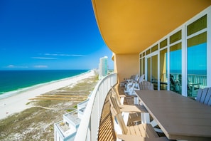 Un balcon avec vue sur une plage et l’océan, un immeuble de grande hauteur à l’horizon et un ciel bleu dégagé.