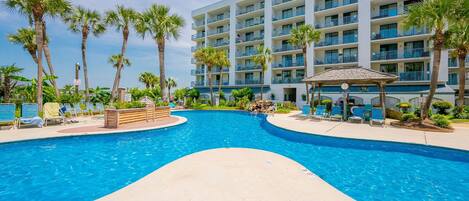 A hotel with a swimming pool, palm trees, and a building with multiple balconies.