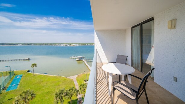 Ein Balkon mit Tisch und Stühlen, mit Blick auf ein Gewässer mit einer Anlegestelle und einer Rasenfläche.
