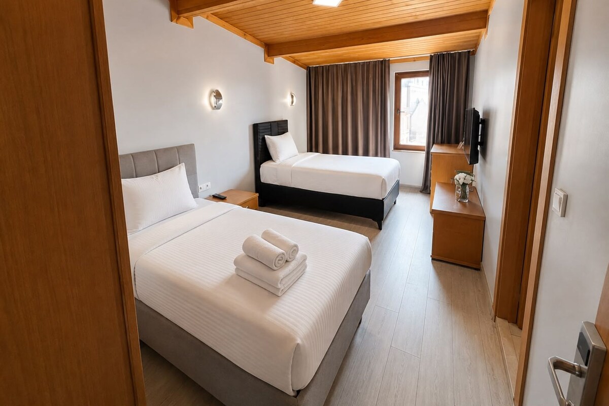 Habitación de hotel con dos camas, techo de madera, ventana con cortinas, mesita de noche y televisor.