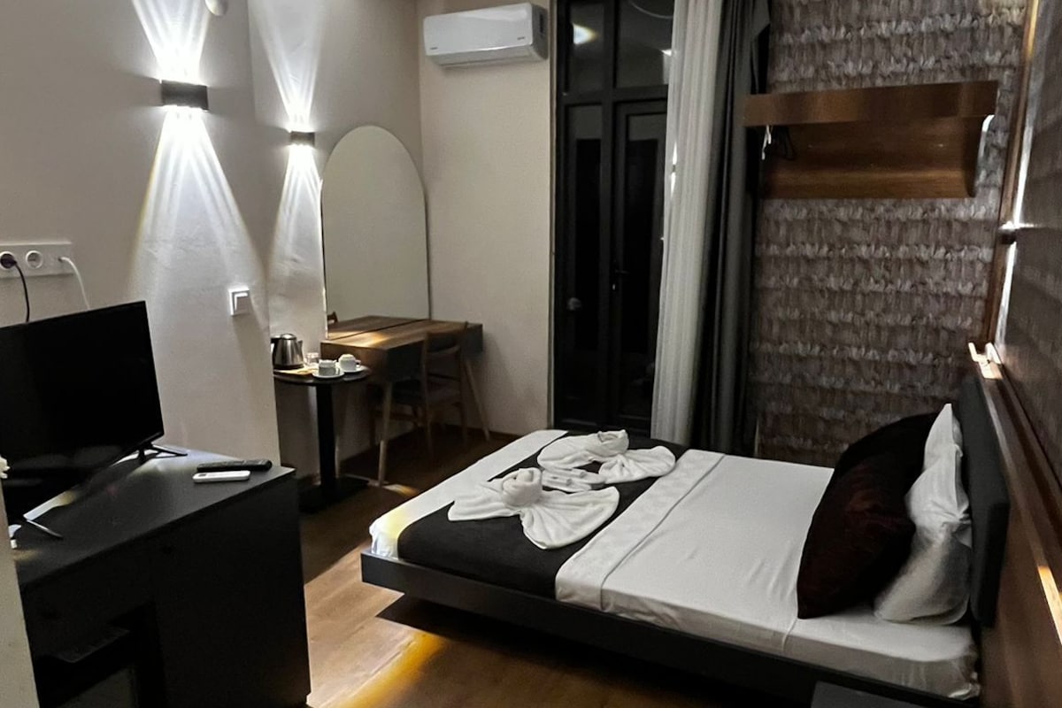 A modern hotel room with a bed, desk, chair, and a TV.