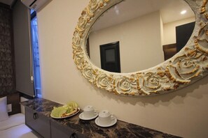 Un baño con encimera de mármol, un espejo grande y ornamentado, y una mesita con tazas y una fuente de fruta.