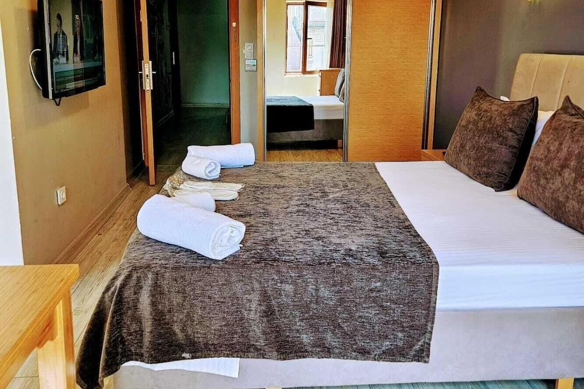 A bedroom with a bed, a wooden ceiling, a TV on the wall, and a bathroom visible through an open door.