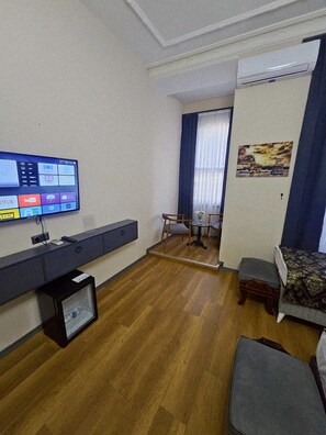 Un espacio habitable compacto con un televisor de pantalla plana montado en la pared, una mesita, un sofá y una ventana con cortinas.