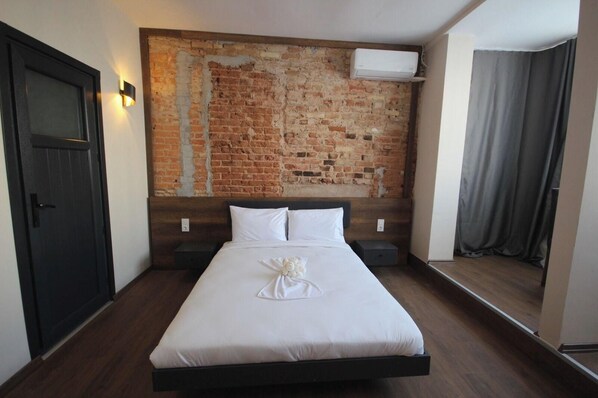 A hotel room with a brick wall, a bed with white linens, a nightstand, a door, and an air conditioning unit. - Taxim 34 (Istanbul)