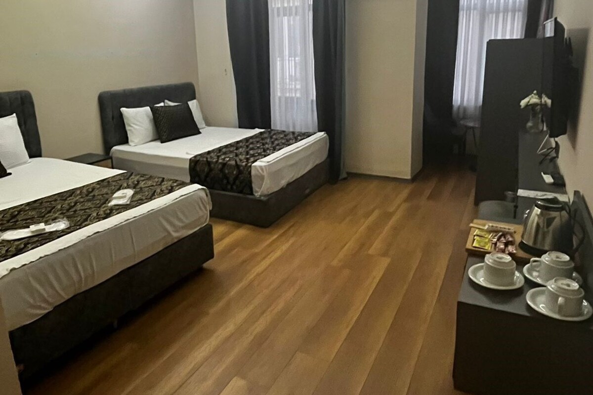 Habitación de hotel con dos camas, una mesita con tetera y tazas, televisión y aire acondicionado.
