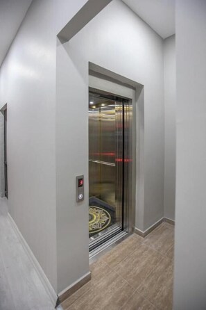 Un ascensor moderno con pantalla digital, situado en un pasillo con paredes de tonos claros y suelo de madera.