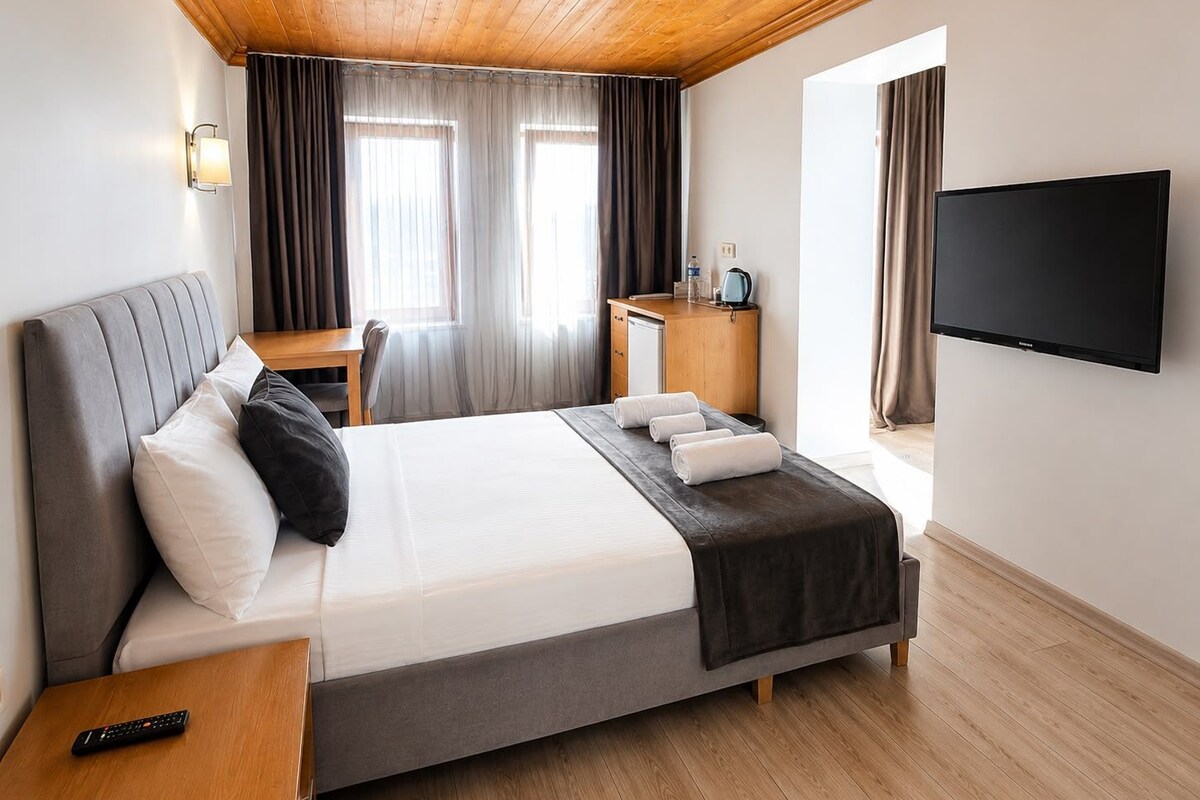 A hotel room with a bed, bedside table, TV, and a desk with a chair.
