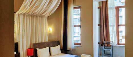 A hotel room with two beds, a wooden ceiling, a window with curtains, a chair, and a nightstand with a lamp.