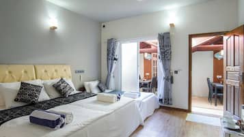 A hotel room with a large bed, a desk, and a dining area visible through an open door.