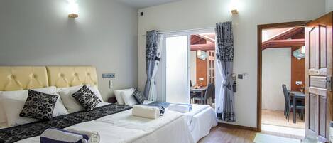 A hotel room with a large bed, a desk, and a dining area visible through an open door.