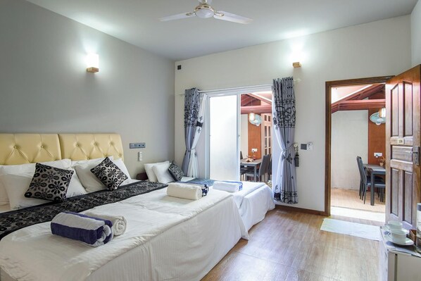 A hotel room with a large bed, a desk, and a dining area visible through an open door. - Palm Oasis At Ukulhas (Ukulhas)