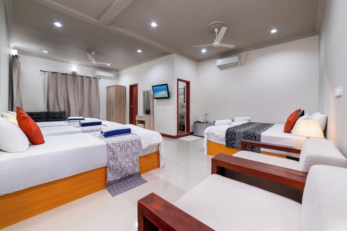 A hotel room with two beds, a sofa, a TV, and a ceiling fan.