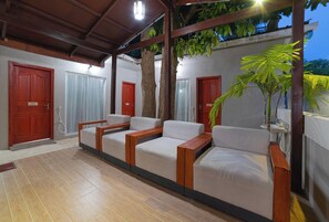 A covered outdoor seating area with a row of white sofas and wooden tables, surrounded by red doors and a potted plant. - Palm Oasis At Ukulhas (Ukulhas)