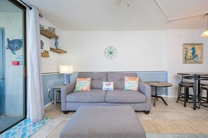 Ein Wohnzimmer mit grauem Sofa, zwei Kissen, einem kleinen Tisch und einem an der Wand befestigten Kompass.